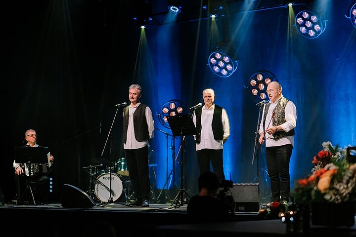 Zdjęcia przedstawia czterech mężczyzn. Trzech śpiewa, jeden gra na akoreonie.