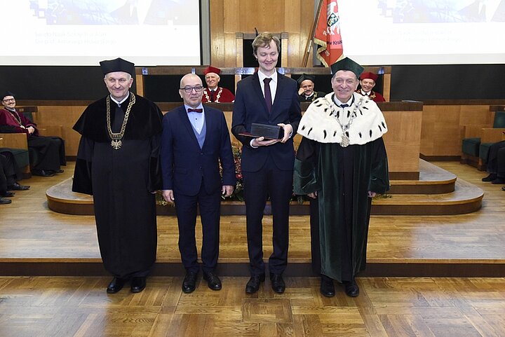 Zdjęcie przedstawia głównie czterech mężczyzn. Dwóch trzyma nagrodę i dyplom.
