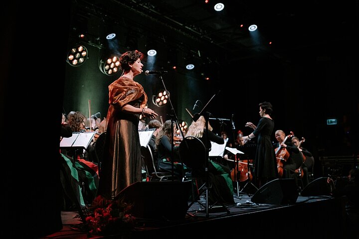 Zdjęcie przedstawia spiewającą kobietę w towarzystwie orkiestry.